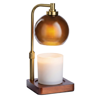 A candle warmer with an amber colored globe above a white candle on a brown wooden pedestal.