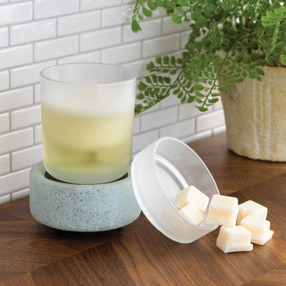 Candle warmer with a glass candle and a bowl of wax cubes on a wooden surface.