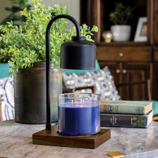 A black dome hovering over a candle sitting on a brown wooden base with books and a plane in the background.
