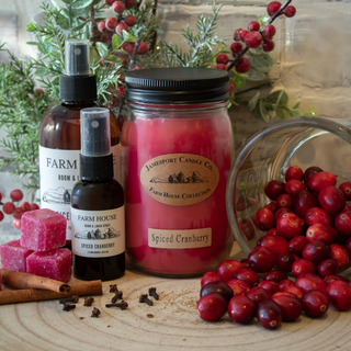 Spiced cranberry candle, soap, and diffuser with cranberries and cinnamon on a wooden surface.